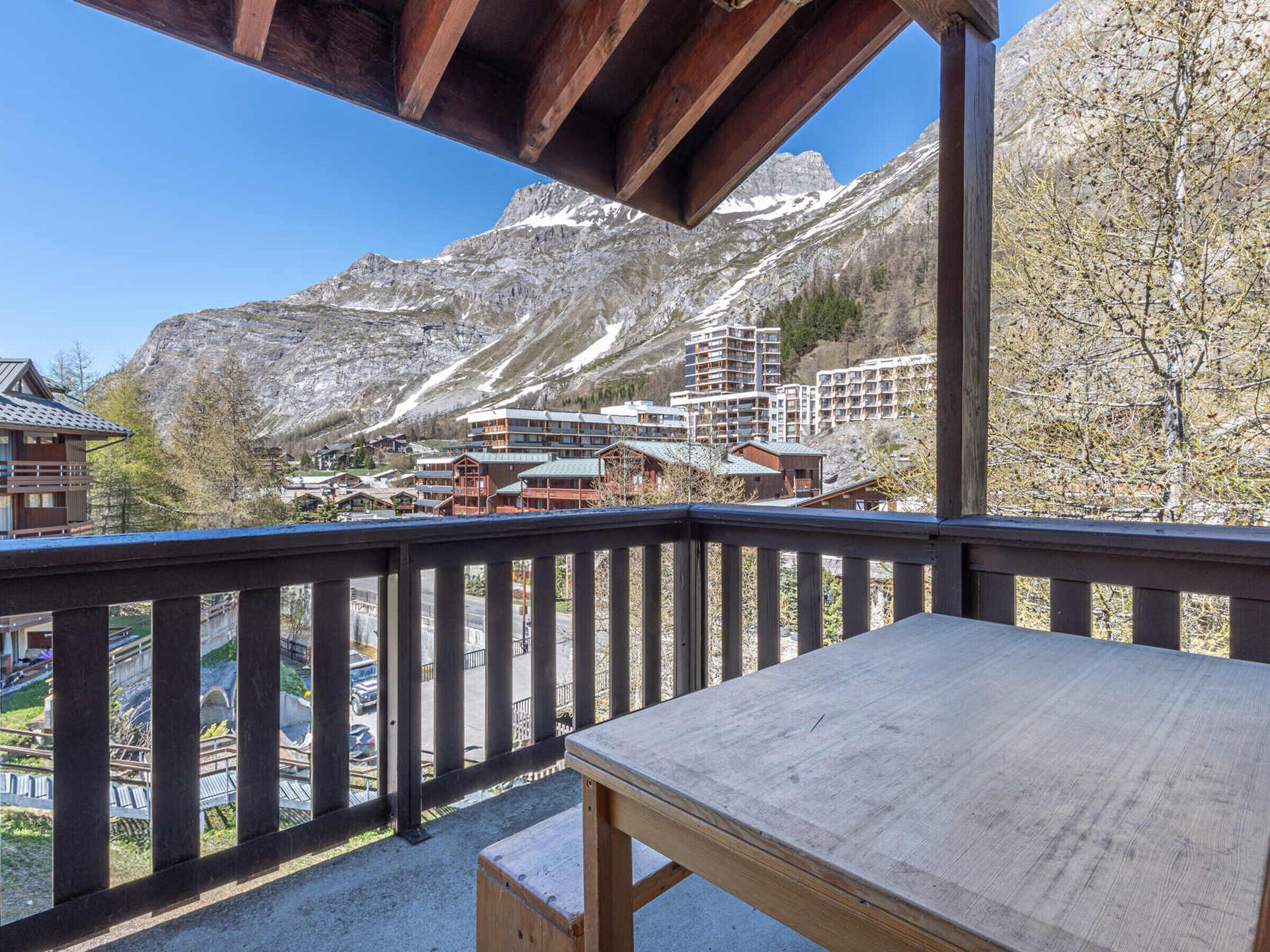 A wooden balcony with a view of a mountain and buildings in the background.