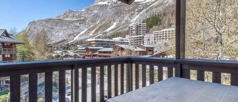A wooden balcony with a view of a mountain and buildings in the background.