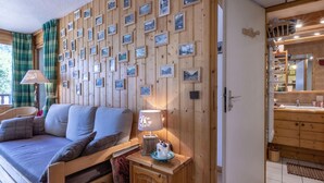 Une pièce chaleureuse avec un mur en bois orné de tableaux encadrés, un lit avec une tête de lit, une table de chevet avec une lampe, et une vue sur la salle de bain, qui est également dotée de meubles en bois.