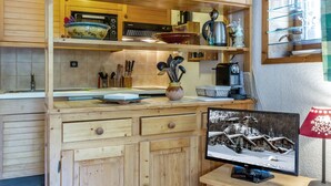 Une cuisine équipée de meubles en bois, d’un four à micro-ondes, d’une bouilloire et d’une machine à café. Une fenêtre offre une vue sur un paysage enneigé.