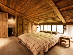 Quarto de madeira com uma cama grande, uma mesa de cabeceira e uma janela.