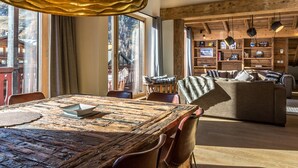 Een rustiek houten interieur met een grote eettafel, lederen stoelen en een gezellige zithoek met een bank en boekenplanken.