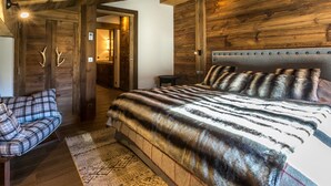 Een slaapkamer met een groot bed, een stoel, houten wanden en een deur versierd met gewei.