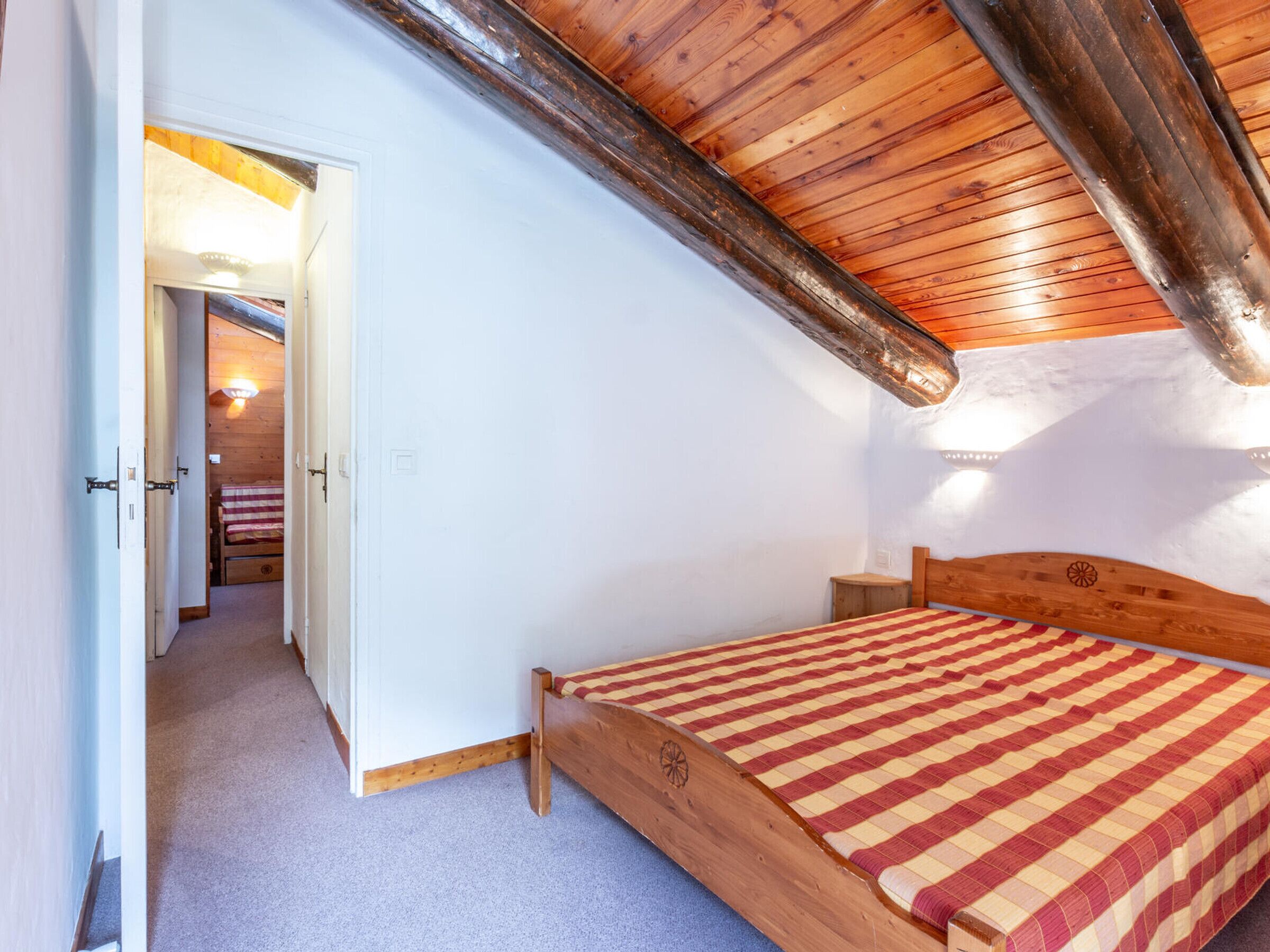 A bedroom with a sloped ceiling, a wooden bed, a nightstand, and a door leading to another room.