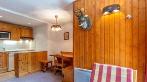 Interior acolhedor de uma cabana com paredes de madeira, área de jantar, cozinha compacta e uma cama com manta xadrez.