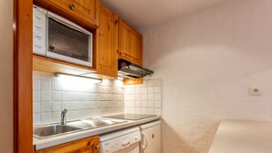 Uma cozinha compacta com armários de madeira, micro-ondas embutido, lava-louças e bancada.