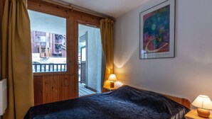 A hotel room with a bed, a nightstand, a lamp, a window with curtains, and a painting on the wall.
