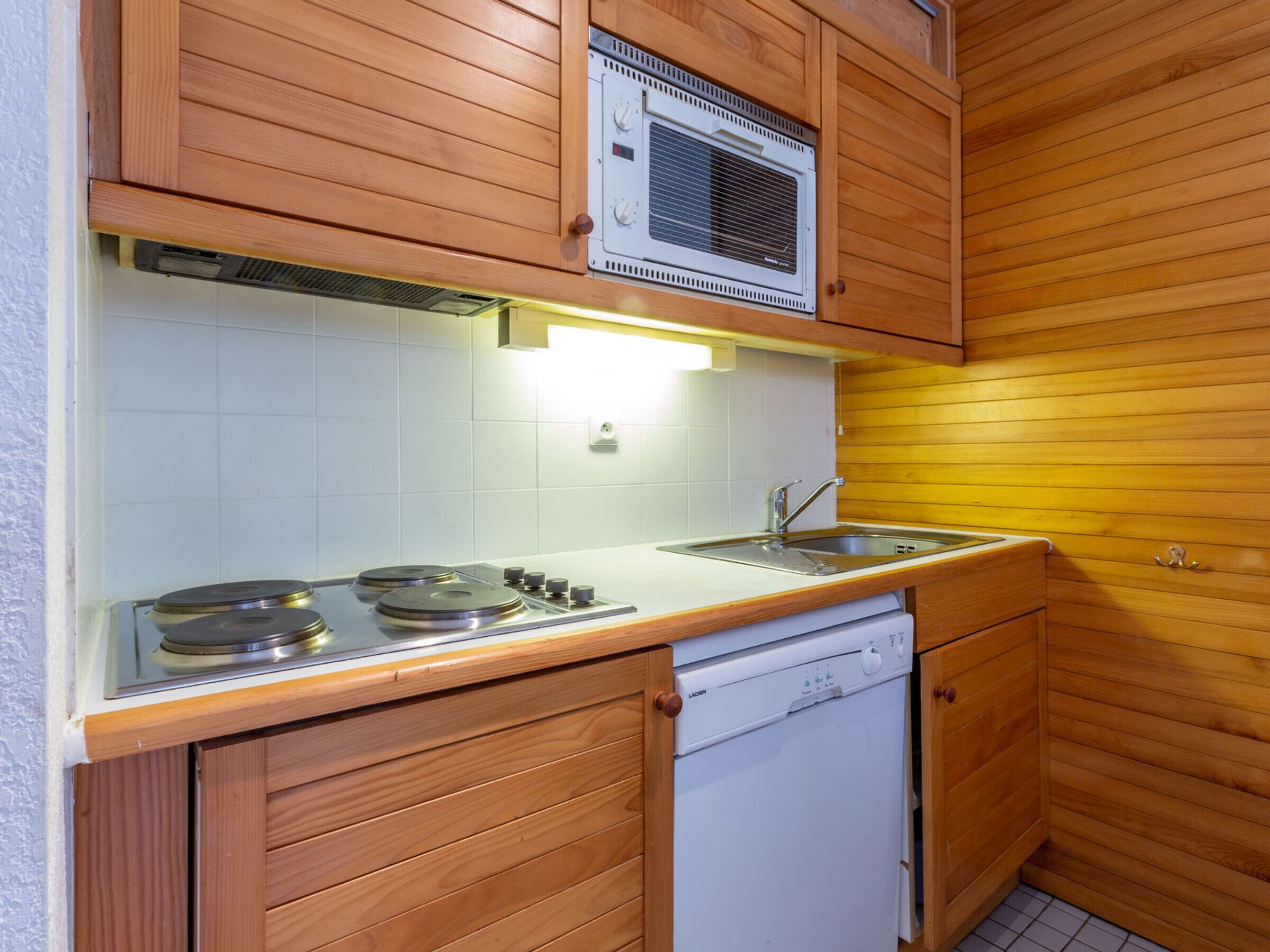 Une cuisine compacte avec des meubles en bois, un four à micro-ondes encastré, une cuisinière et un lave-vaisselle.