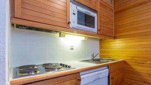 A compact kitchen with wooden cabinets, a built-in microwave, a stove, and a dishwasher.