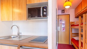 A compact kitchenette with a microwave, sink, and small refrigerator. There is a bunk bed with red bedding and a wooden ladder. - Cozy ski-in studio, 3 ppl, La Daille, Val-d'Isère (Val-d'Isère)