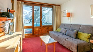 A cozy living room with a wooden sofa, a small table, and a view of snowy mountains through large glass doors. - Cozy ski-in studio, 3 ppl, La Daille, Val-d'Isère (Val-d'Isère)