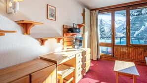 A cozy room with a wooden desk, a TV, and a view of snowy mountains through large windows. - Cozy ski-in studio, 3 ppl, La Daille, Val-d'Isère (Val-d'Isère)