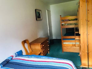 Una habitación con una cama litera, un escritorio de madera, una silla, un aparador y un cuadro en la pared.