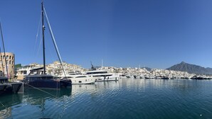 Un port de plaisance où sont amarrés de nombreux yachts, avec en arrière-plan un paysage montagneux et un ciel bleu dégagé.
