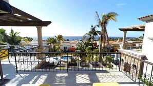 Varanda com vista para o mar, palmeiras e piscina.