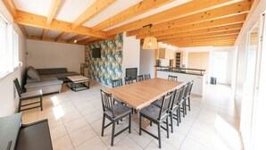 Un vaste espace de vie doté d’un plafond en bois, d’une table à manger avec des chaises, d’un canapé et d’une cuisine à l’arrière-plan.