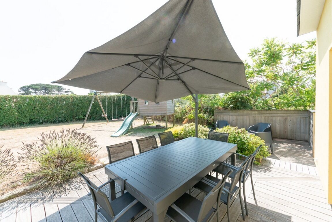 Eine Terrassengruppe mit Tisch und Stühlen, ein großer Sonnenschirm und eine Rutsche im Hintergrund.