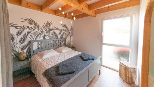 Une chambre à coucher comprenant un lit, une table de chevet, un luminaire fixé au mur, une fenêtre et un panier en osier.