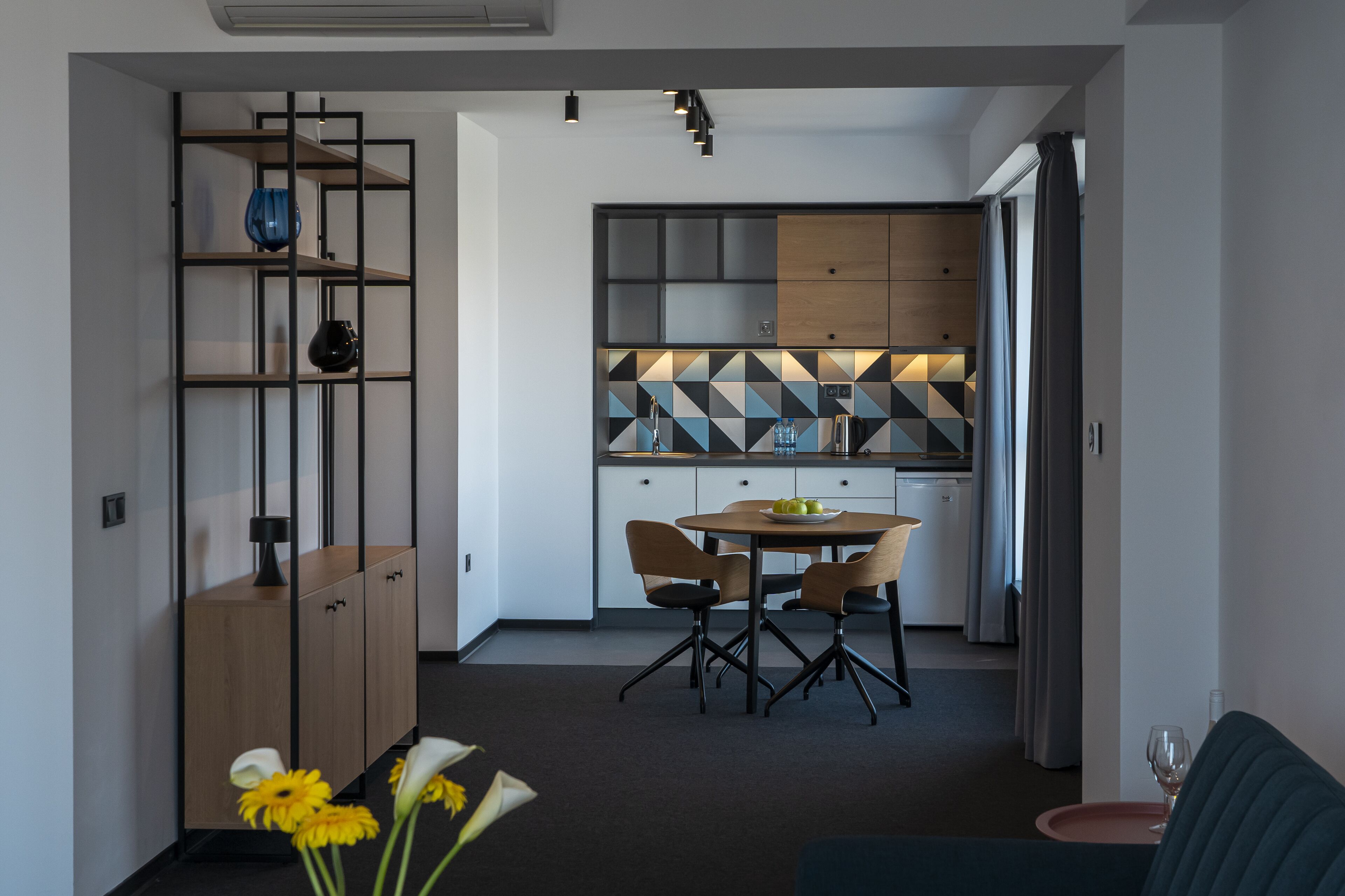 Una cocina moderna con un salpicadero geométrico, un comedor con mesa y sillas redondas, y una sala de estar con sofá y mesa de centro.