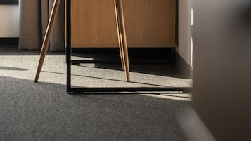 Un hotel moderno con un escritorio de madera, un sillón tapizado en gris y vistas de la ciudad desde la ventana.