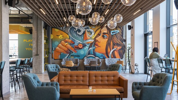 A modern lounge area with a large mural, comfortable seating, and a view of the city.