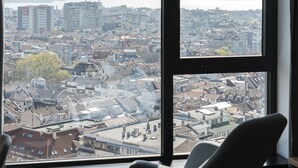 A room with a large window offering a city view, a rocking chair, and a carpeted floor.