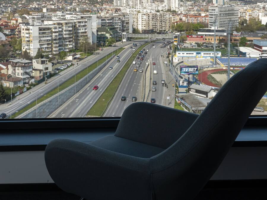 A cityscape view from a window with a rocking chair in the foreground.