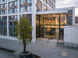 A modern building with large windows, a glass entrance, and a tree in the foreground. - Campus 90 (Varna)