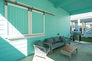 A covered patio area with a turquoise exterior, wicker furniture, and a barbecue grill. - Barnacle House by Miss Kitty’s (Rockport)