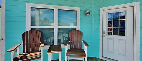A turquoise exterior with two wooden Adirondack chairs and a white door.