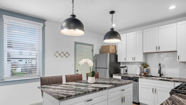 Una cocina moderna con armarios blancos, una isla de mármol e iluminación colgante.