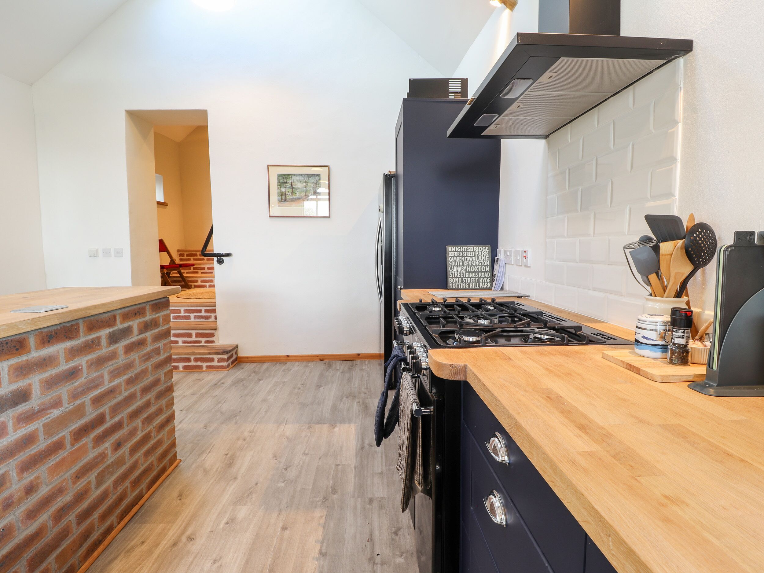 A modern kitchen with a brick accent wall, a gas stove, and a wooden countertop.