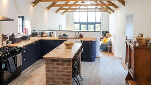 A spacious kitchen with a large island, wooden beams, and a view to the outside. - Mill Cottage (Newport)