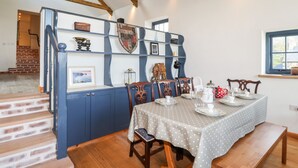 A dining area with a table set for four, wooden chairs, a bench, and a decorative shield on the wall. - Mill Cottage (Newport)