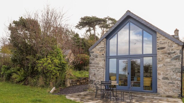 A stone house with a large glass window and a patio with outdoor furniture. - Mill Cottage (Newport)