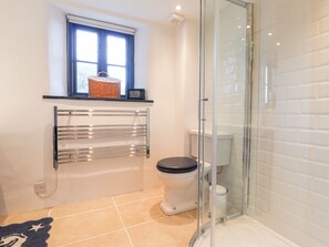 A bathroom with a glass-enclosed shower, a toilet, and a towel rack with a basket on top. - Mill Cottage (Newport)