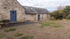 A stone building with a sloped roof, a blue door, and a gravel driveway. - Mill Cottage (Newport)