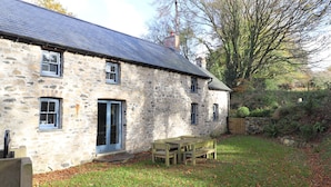 A stone house with a tiled roof, a wooden door, and a small porch with a bench. - Castle Coach House (Newport)