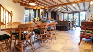 A spacious kitchen with wooden beams, a dining area with wooden chairs and a table, and large windows offering a view of the outdoors. - Castle Coach House (Newport)