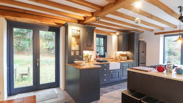 A modern kitchen with dark cabinetry, a central island, and a stone-tiled floor. - Castle Coach House (Newport)