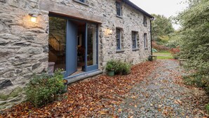 A stone house with a wooden staircase leading to a door, a garden path with fallen leaves, and a small bench. - Castle Coach House (Newport)