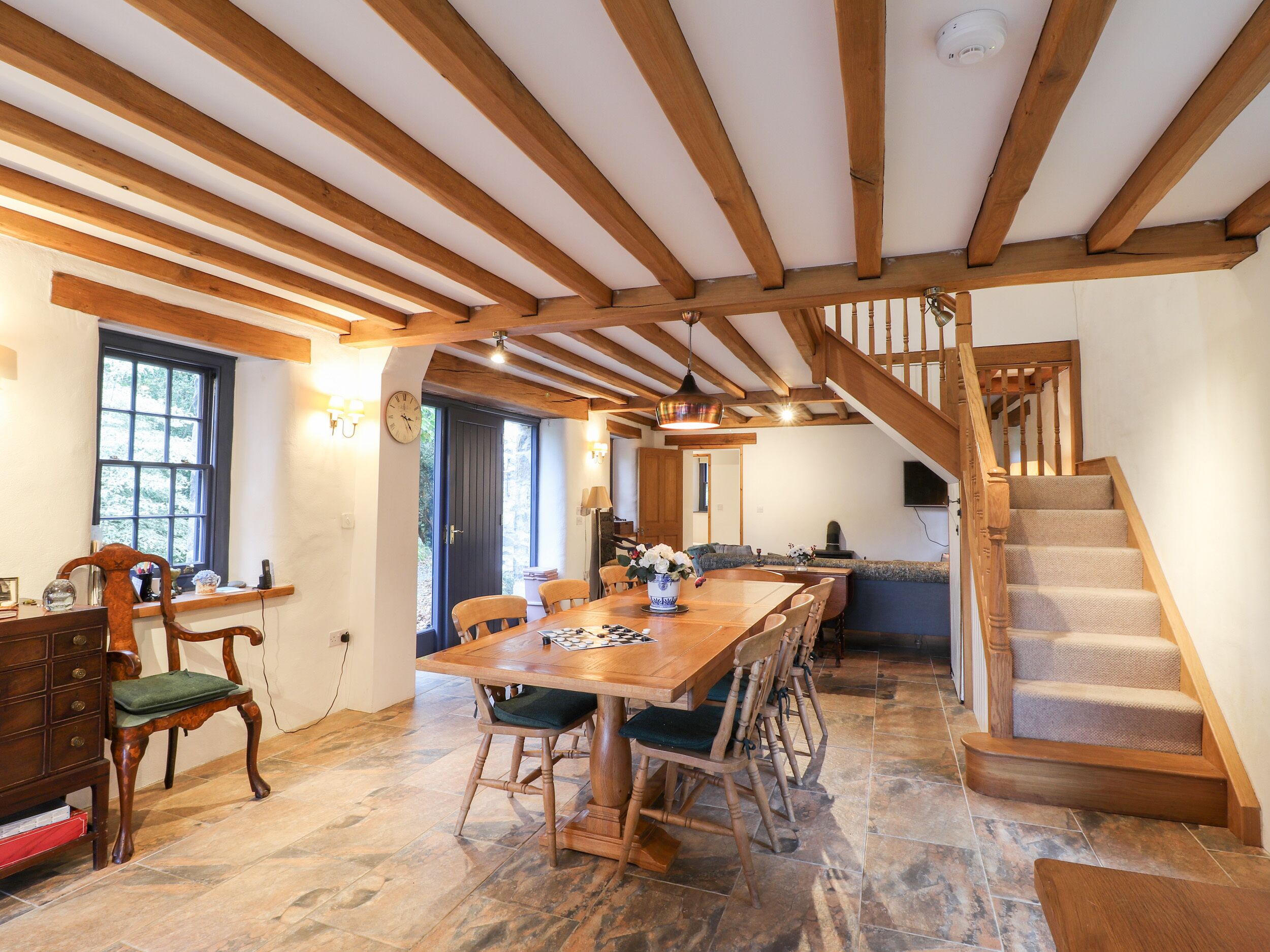 A spacious dining area with a wooden table and chairs, a staircase, and a view of the outdoors.