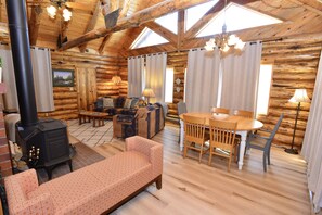 A log cabin interior with a fireplace, sofa, dining table, and chairs.