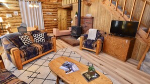 A cozy log cabin interior with a sofa, armchair, wooden coffee table, fireplace, and a television.