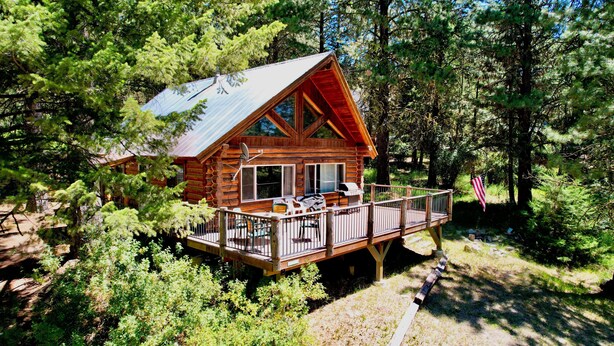 A log cabin with a deck, surrounded by dense forest.