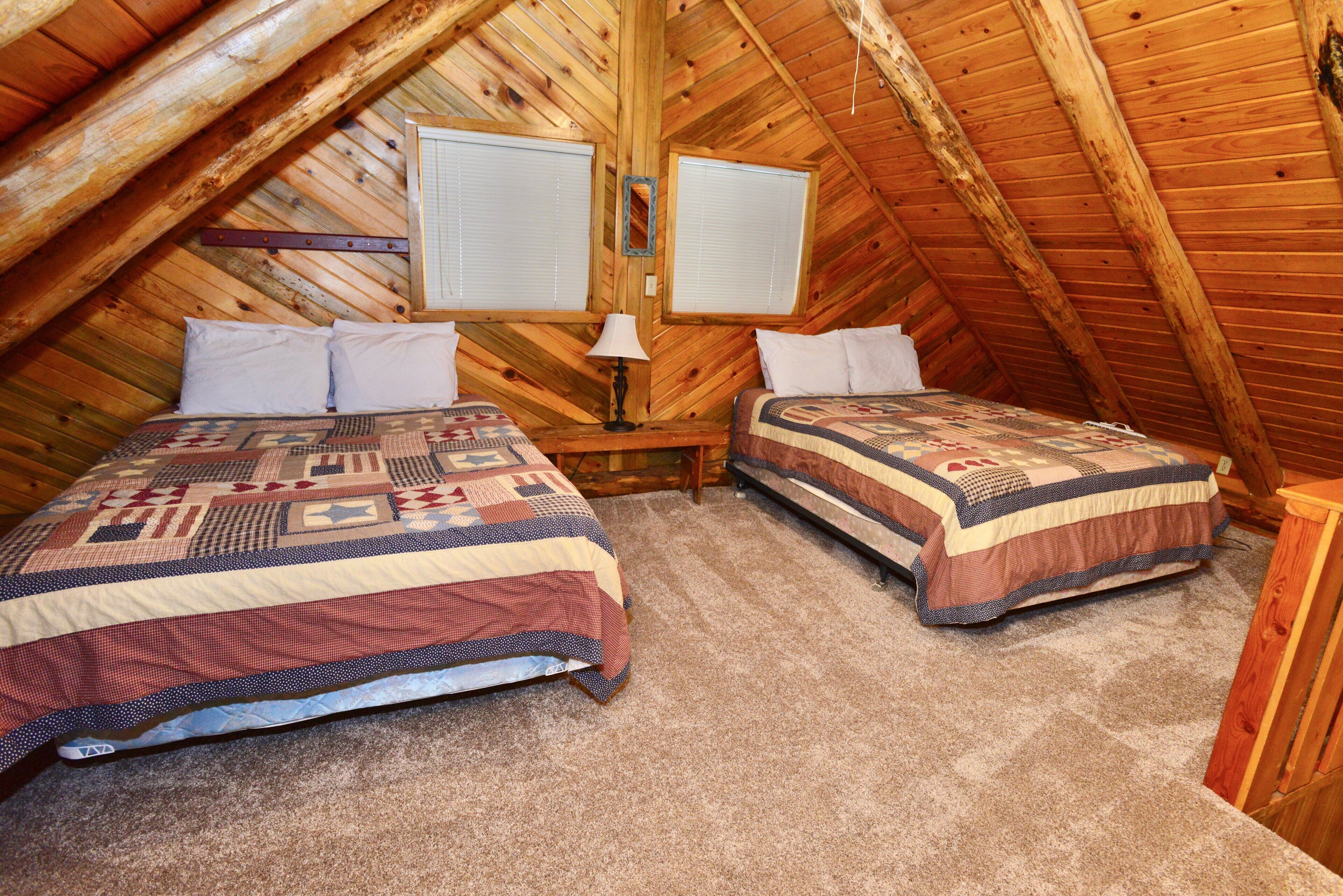 A cozy attic bedroom with two beds, wooden walls, and a sloped ceiling.