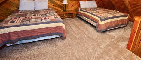 A cozy attic bedroom with two beds, wooden walls, and a sloped ceiling.