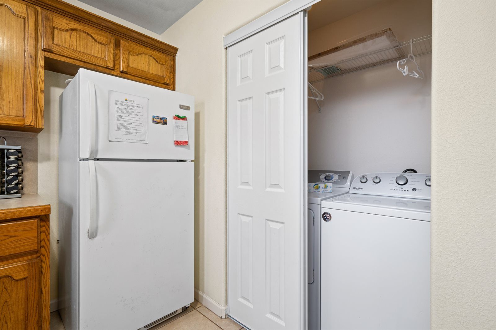 Une cuisine de taille réduite, avec un réfrigérateur blanc, des meubles de rangement en bois, ainsi qu’un lave-linge et un sèche-linge Whirlpool.