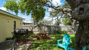 A backyard with a barbecue grill, picnic table, and a blue chair. - Coastal Soul by Miss Kitty’s (Aransas Pass)