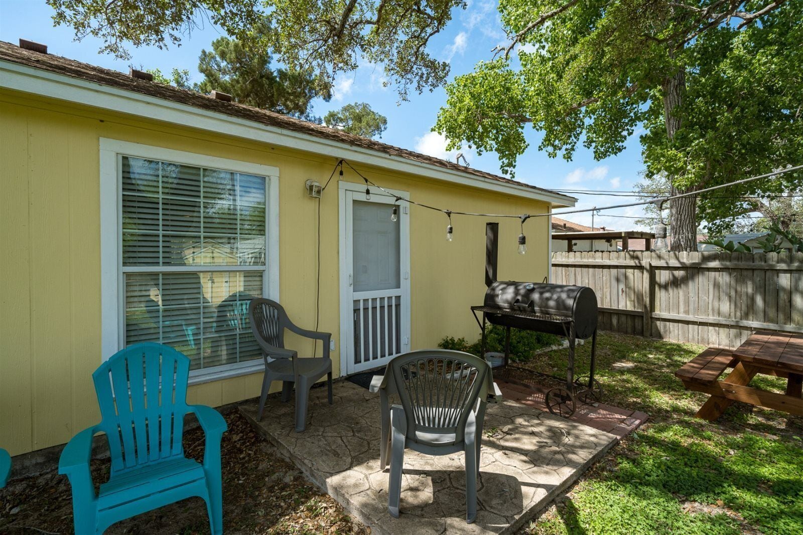 A backyard with a barbecue grill, two plastic chairs, a picnic table, and a wooden fence.